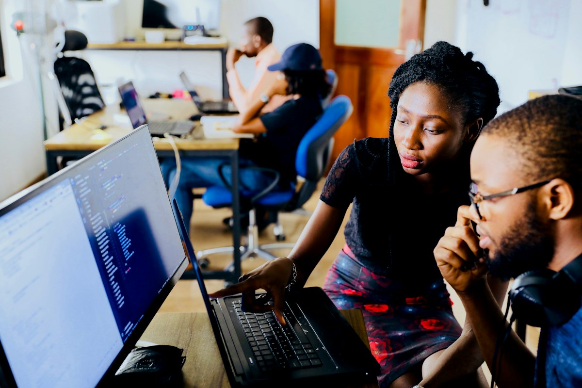 African tech engineers and interns collaborating around monitors in a tech office
